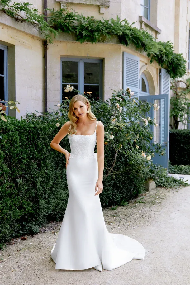 A woman in a white wedding dress is standing in front of a brick wall.