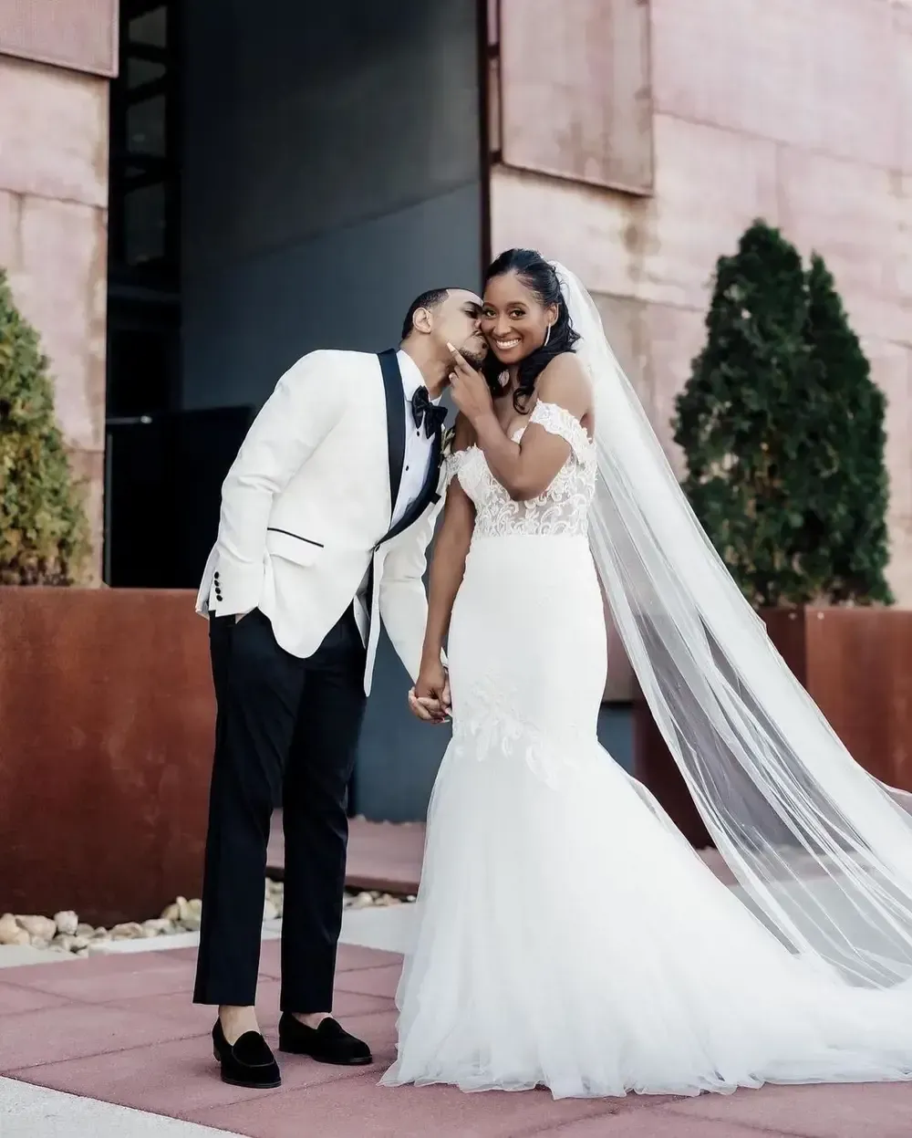 A bride and groom are kissing in front of a building.