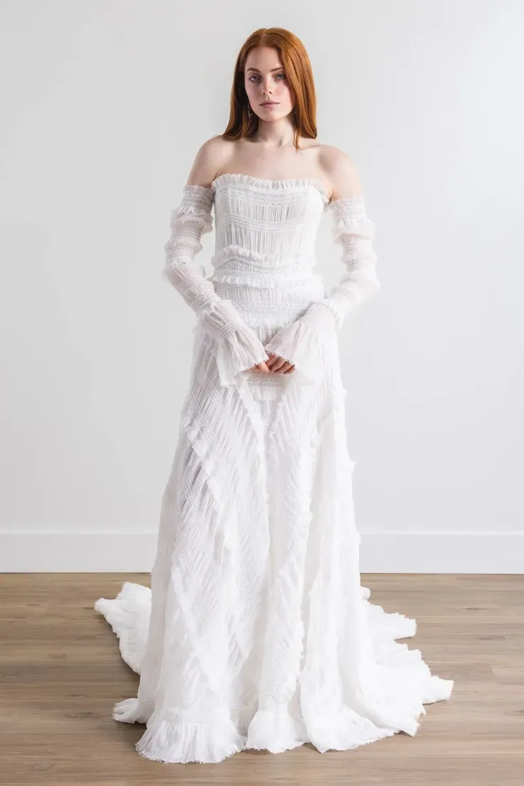 A woman in a white wedding dress and gloves is standing on a wooden floor.