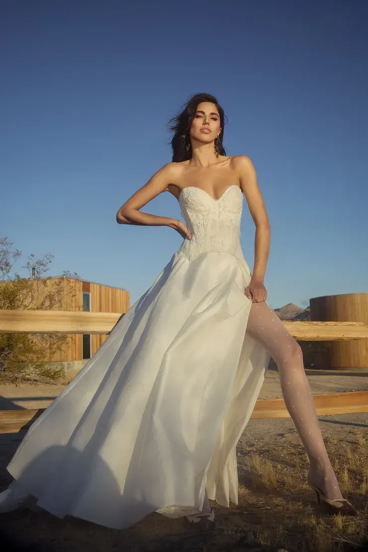 A woman in a white dress is standing next to a wooden fence.