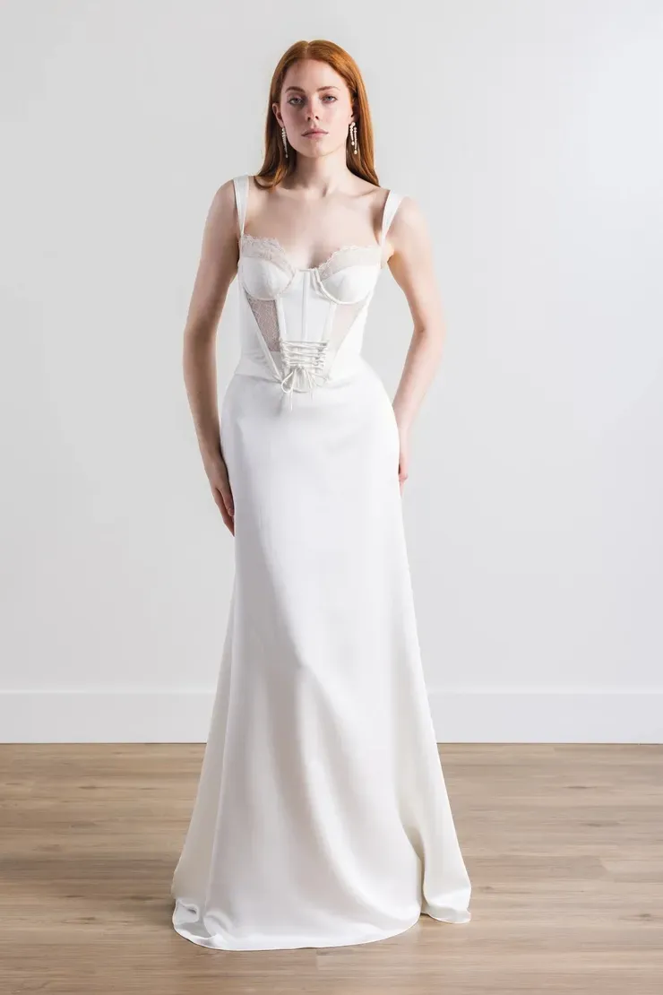 A woman in a white wedding dress is standing on a wooden floor.