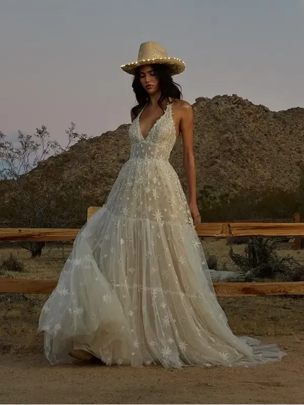 A woman in a wedding dress and cowboy hat is standing in front of a wooden fence.
