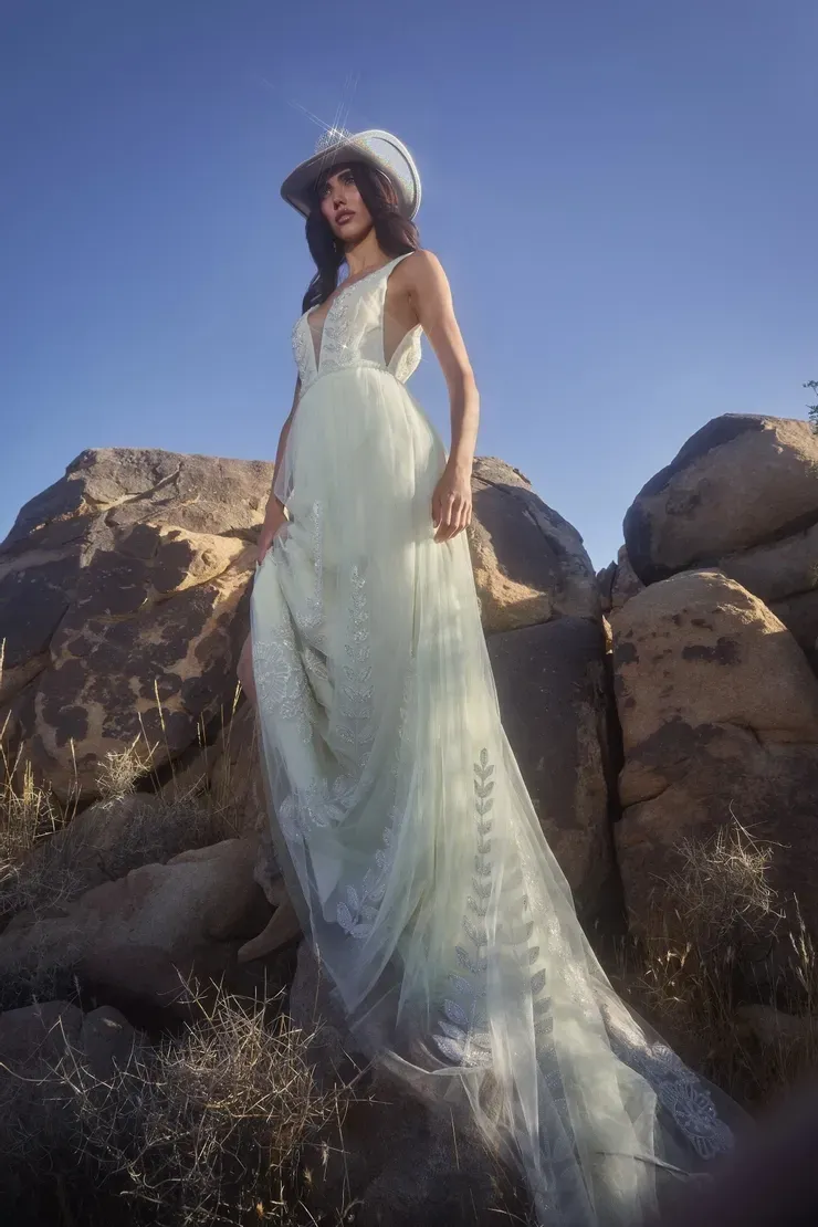 A woman in a white dress and hat is standing on a rock in the desert.