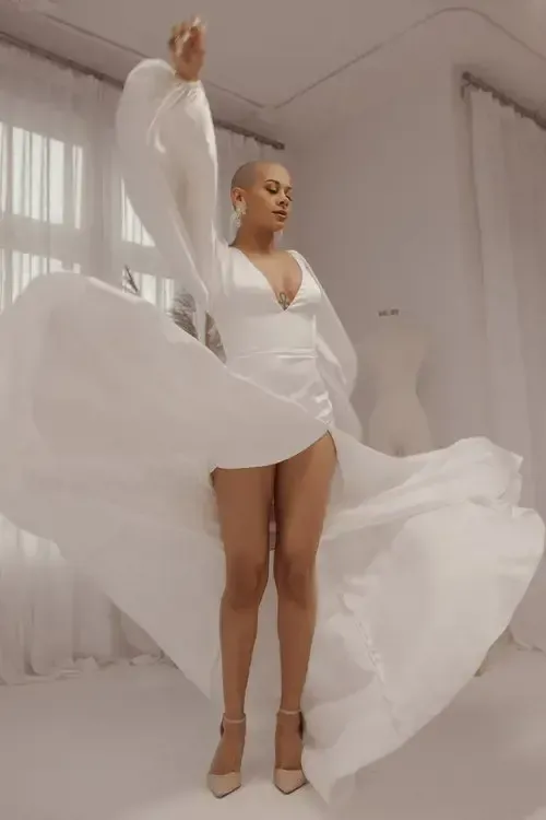 A woman in a white dress is standing in a white room.