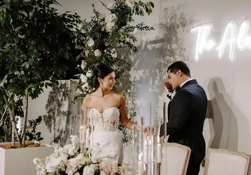 A bride and groom are standing next to each other at a long table.