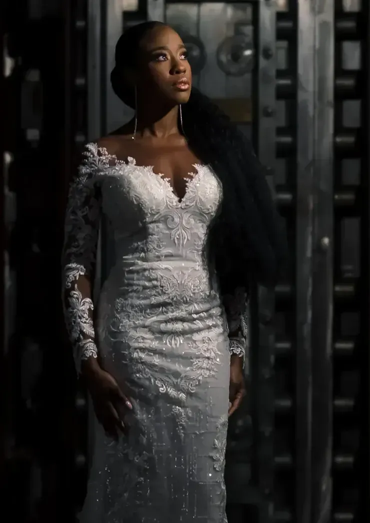 A woman in a wedding dress is standing in front of a vault door.