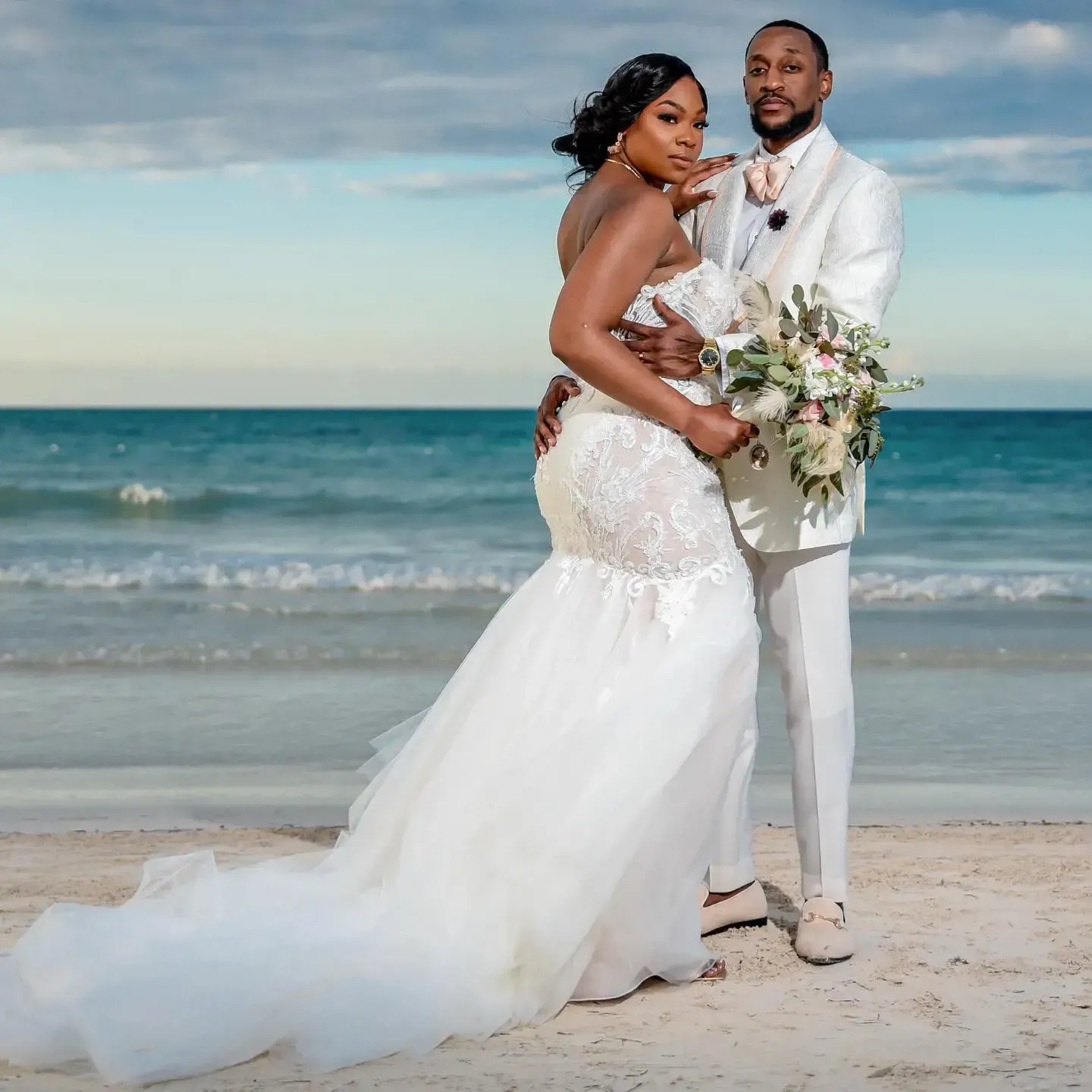 A bride and groom are posing for a picture on the beach.