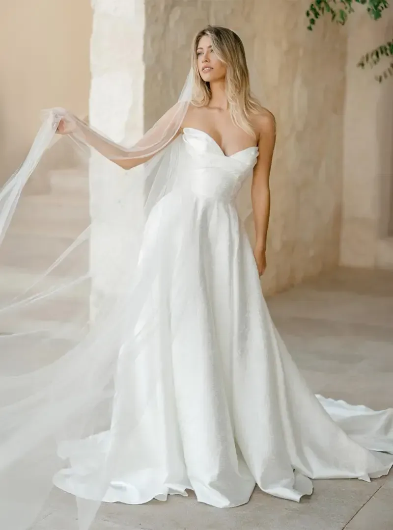 A woman in a white wedding dress and veil is standing in front of a building.