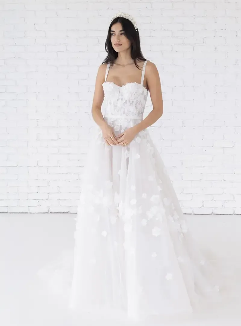 A woman in a white wedding dress is standing in front of a white brick wall.