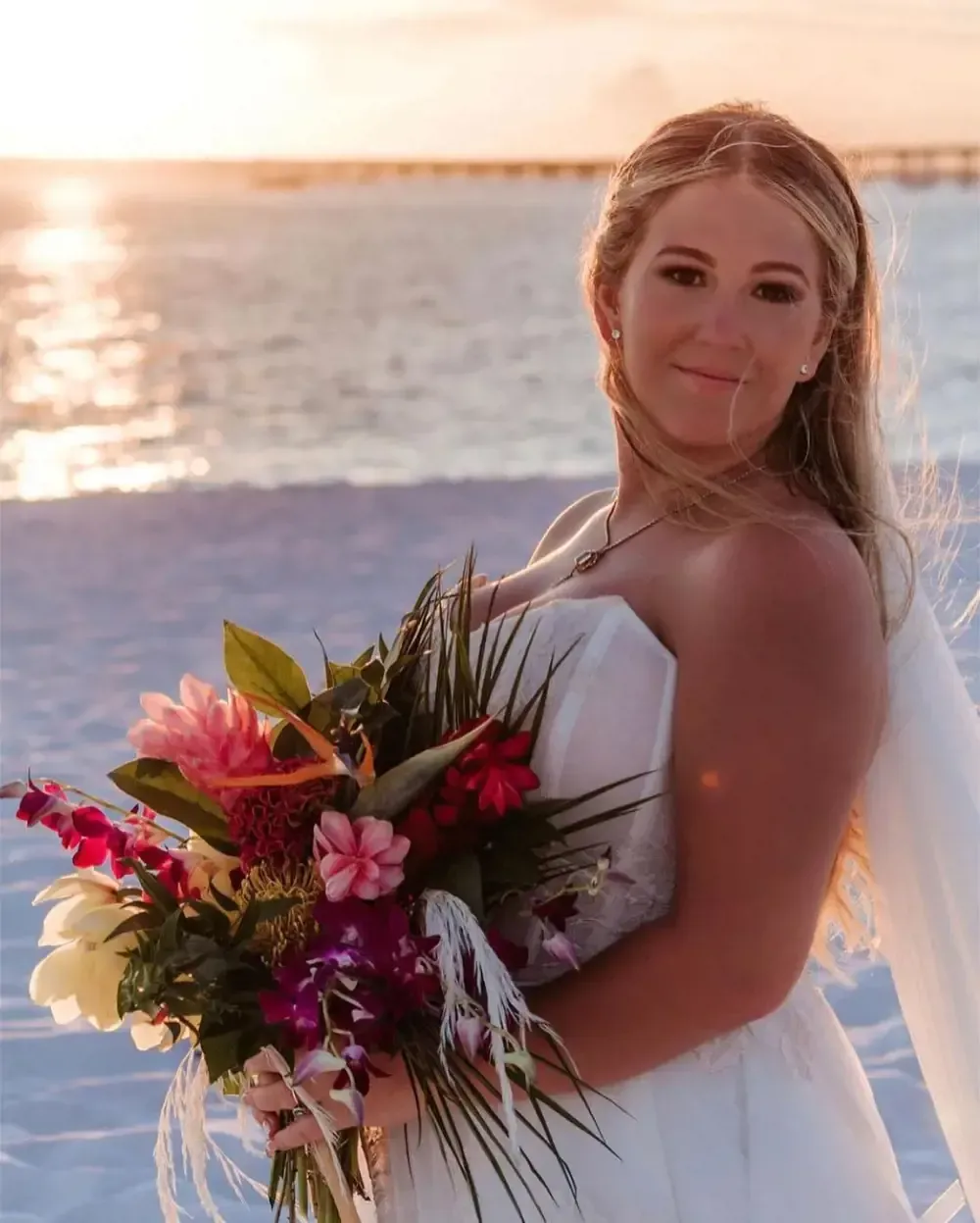 A bride in a wedding dress is holding a bouquet of flowers on the beach.