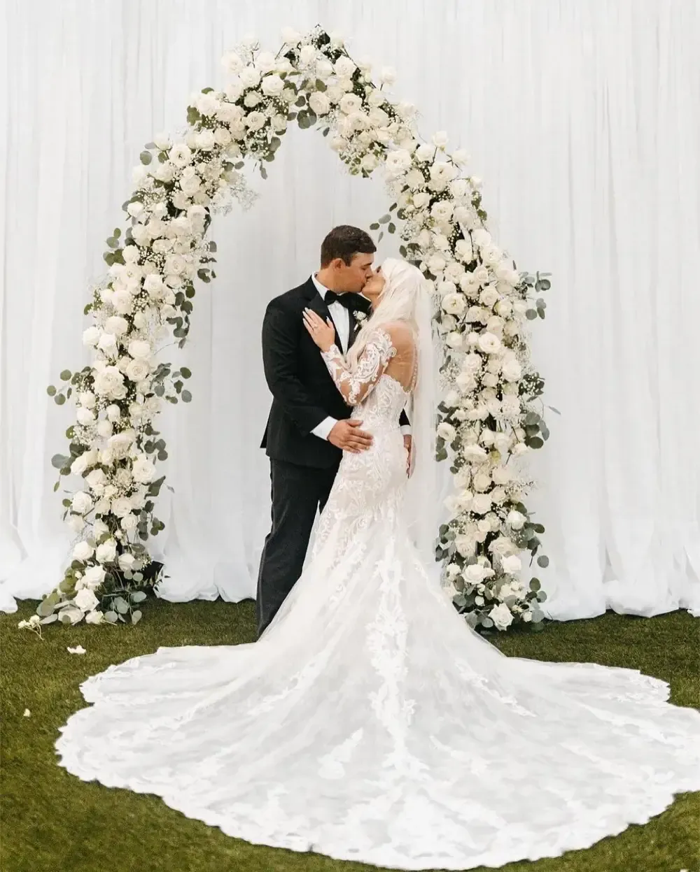 A bride and groom are kissing under a floral arch.