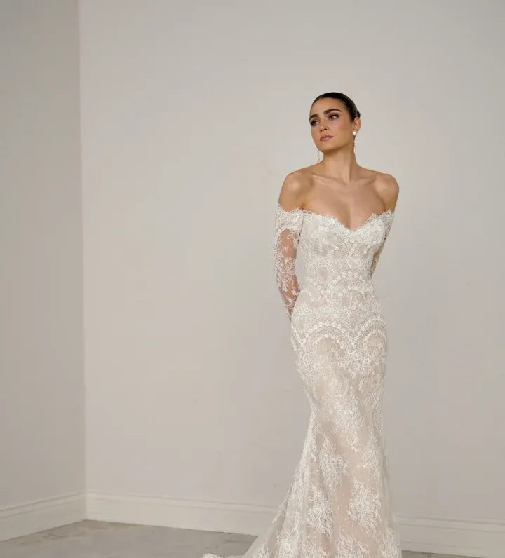 A woman in a white dress is leaning against a wall.