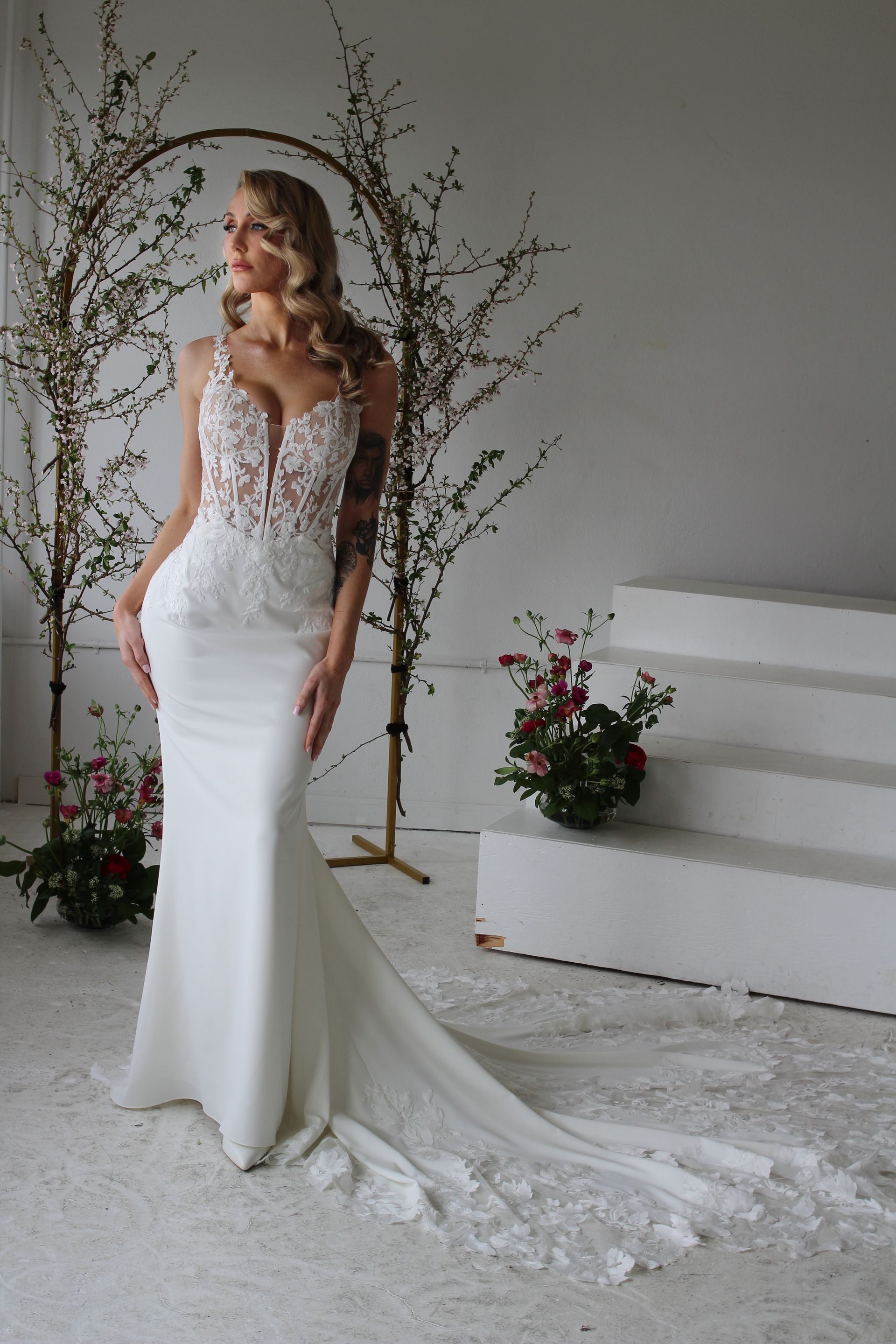 Woman in strapless lace wedding dress with a train, standing in a modern building.