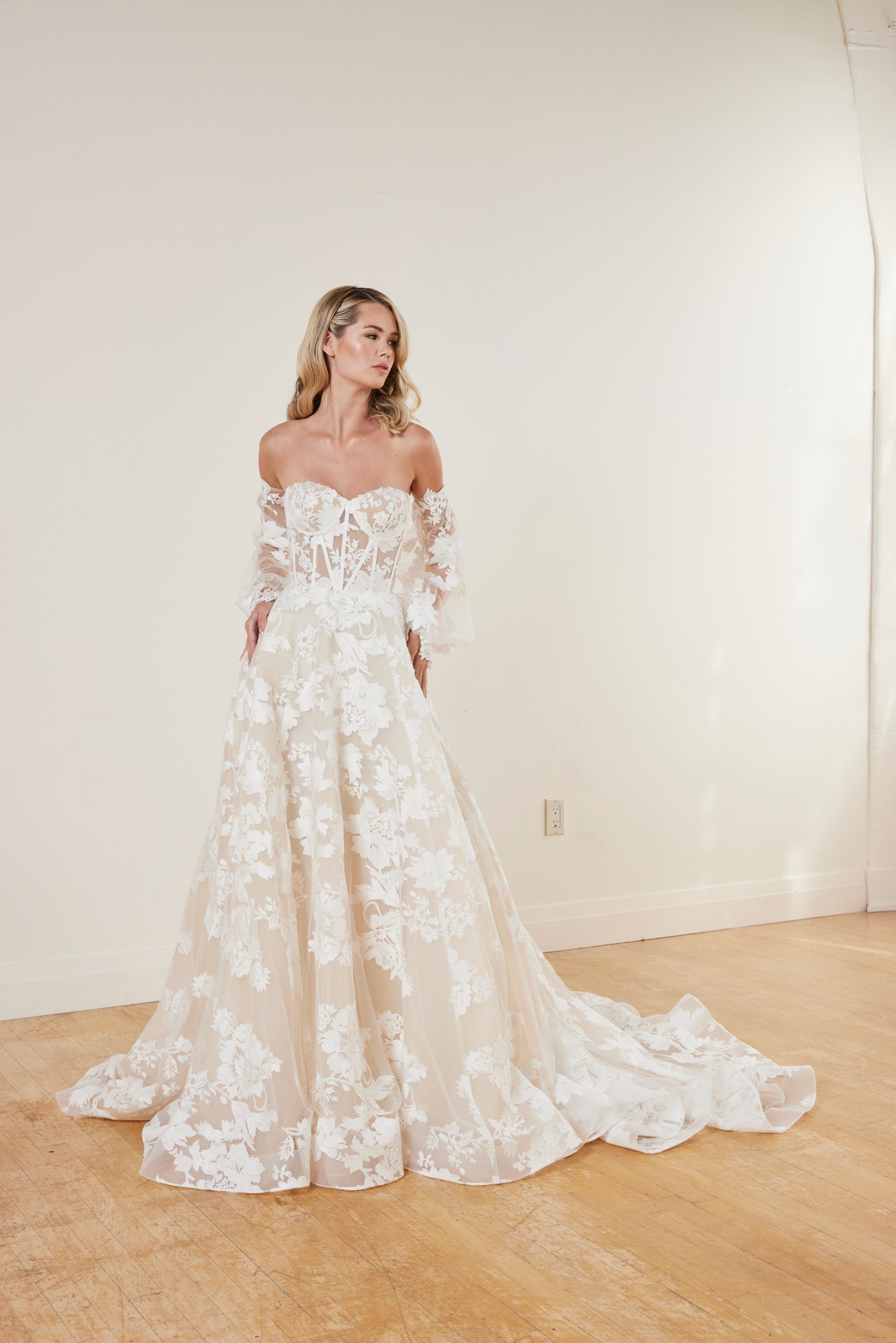 Woman in a white strapless ball gown, standing in a bright interior space with large windows.