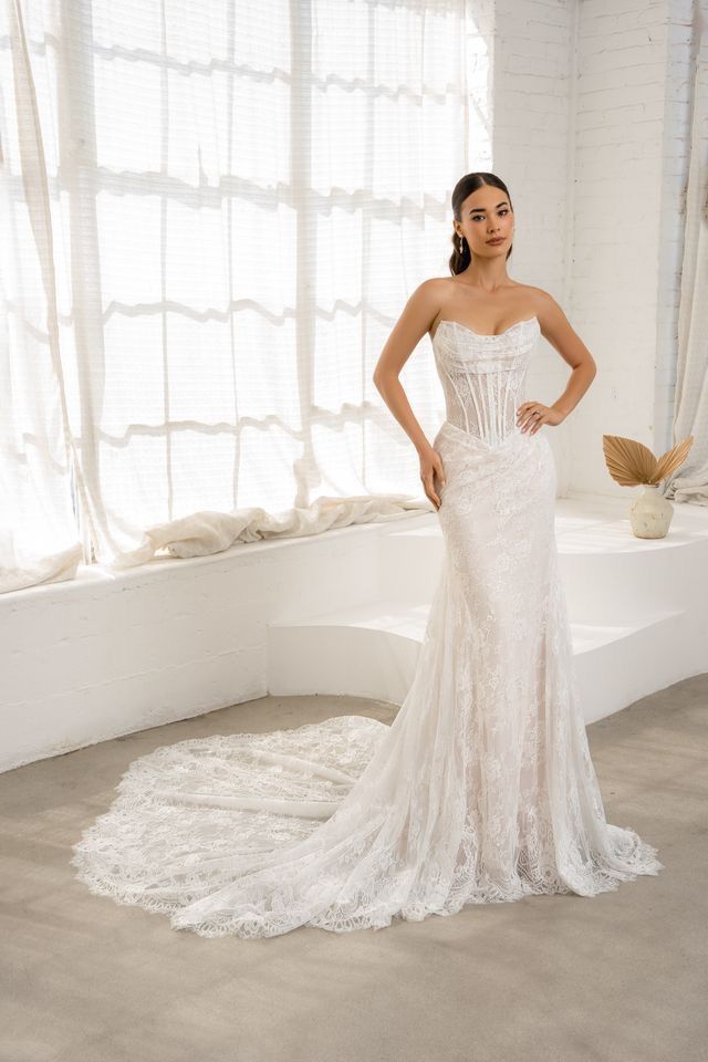 A woman is wearing a white off the shoulder wedding dress with a high slit.