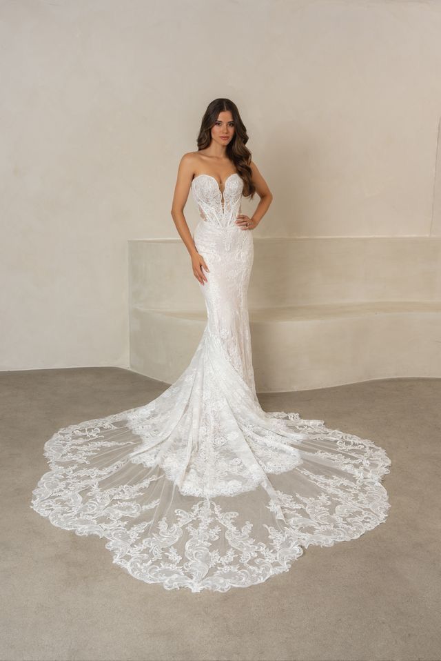 A woman in a white wedding dress is standing in front of a white building.