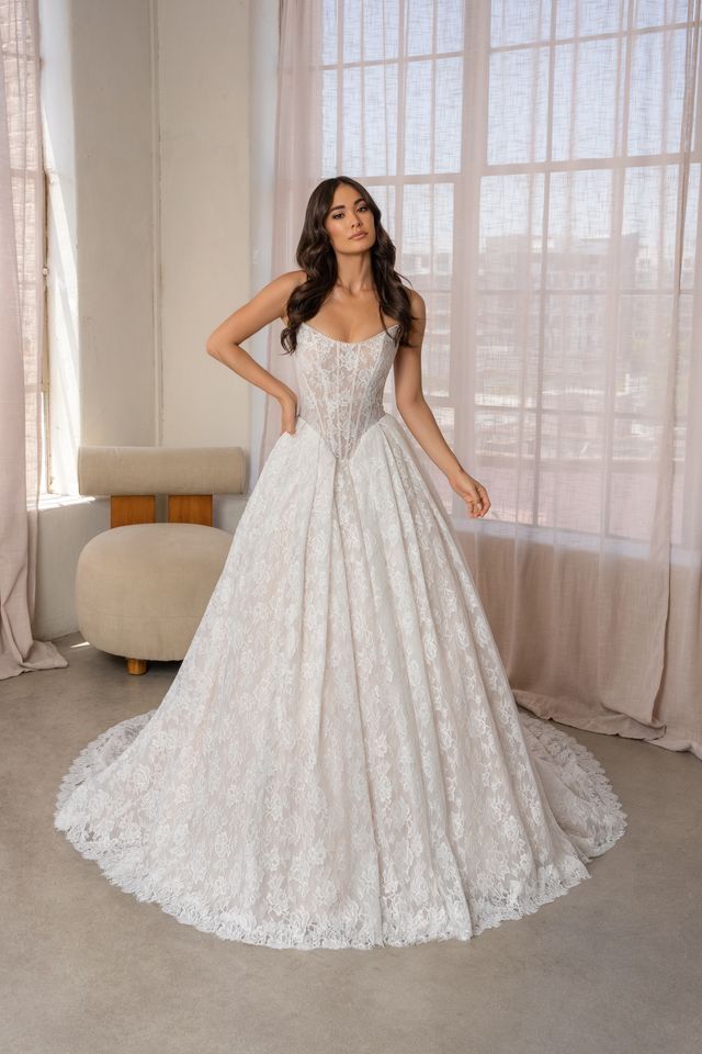 A woman in a white wedding dress is standing in front of a white wall.