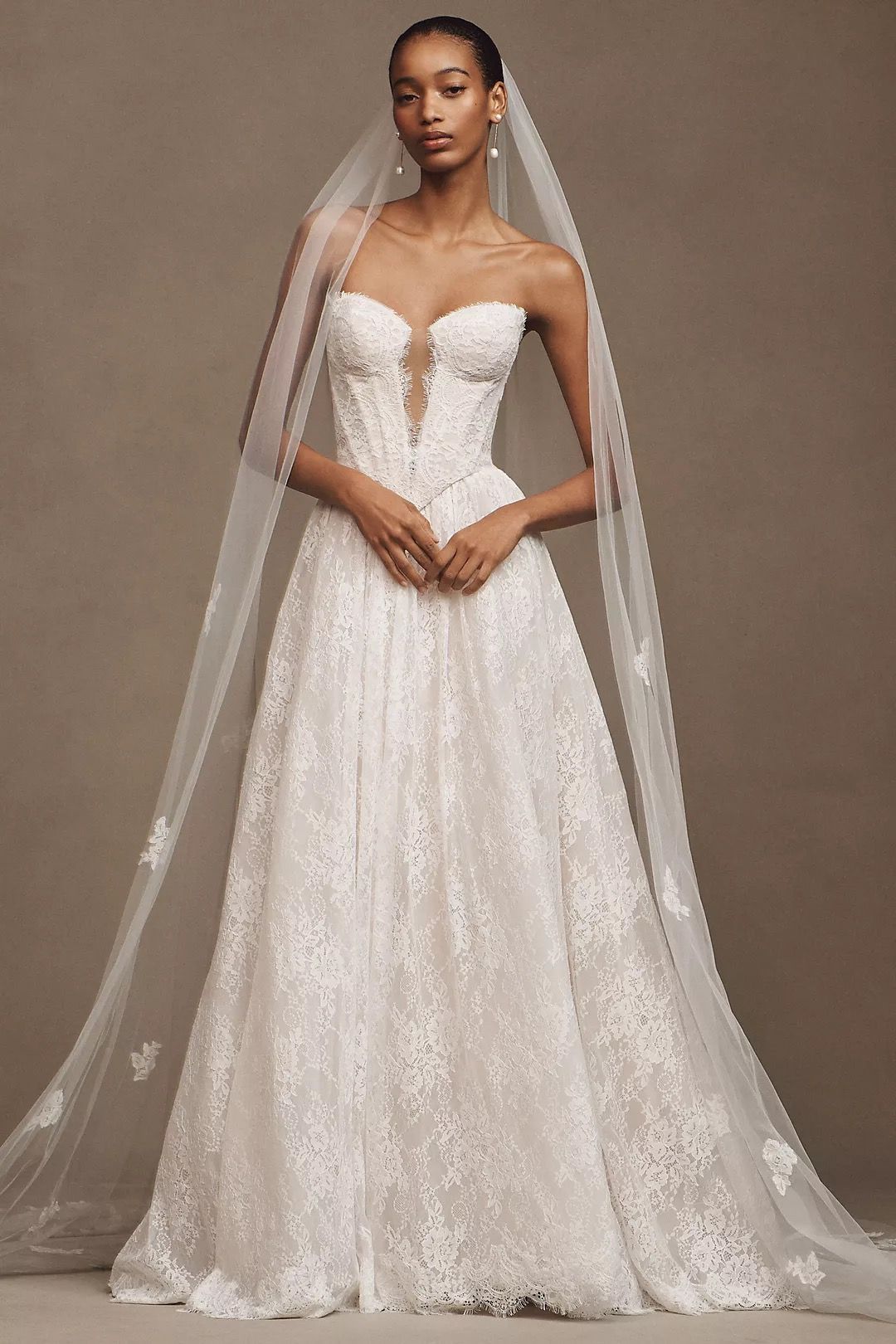 A woman in a white wedding dress is standing in front of a wall.