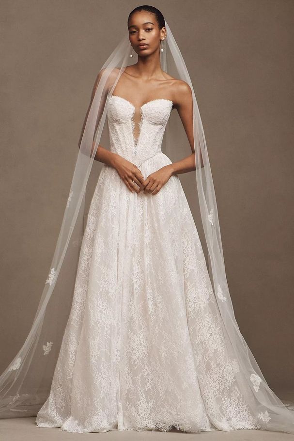 A woman in a white wedding dress is standing in front of a wall.