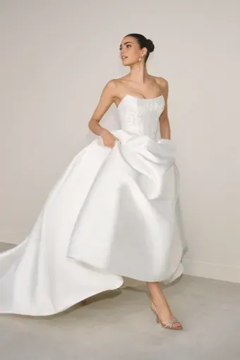 Woman in strapless white wedding dress, walking, pulling up skirt, neutral background.