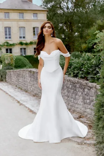 Woman in white off-the-shoulder wedding gown poses outdoors.
