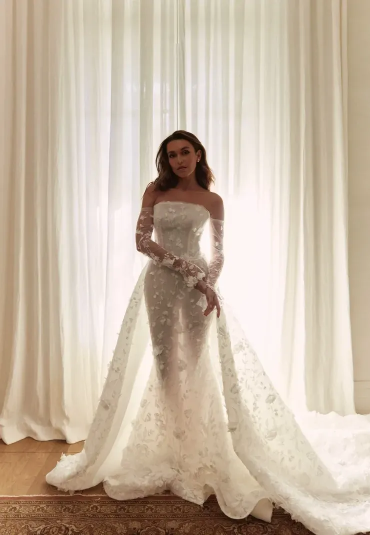 A woman in a wedding dress is standing in front of a window.