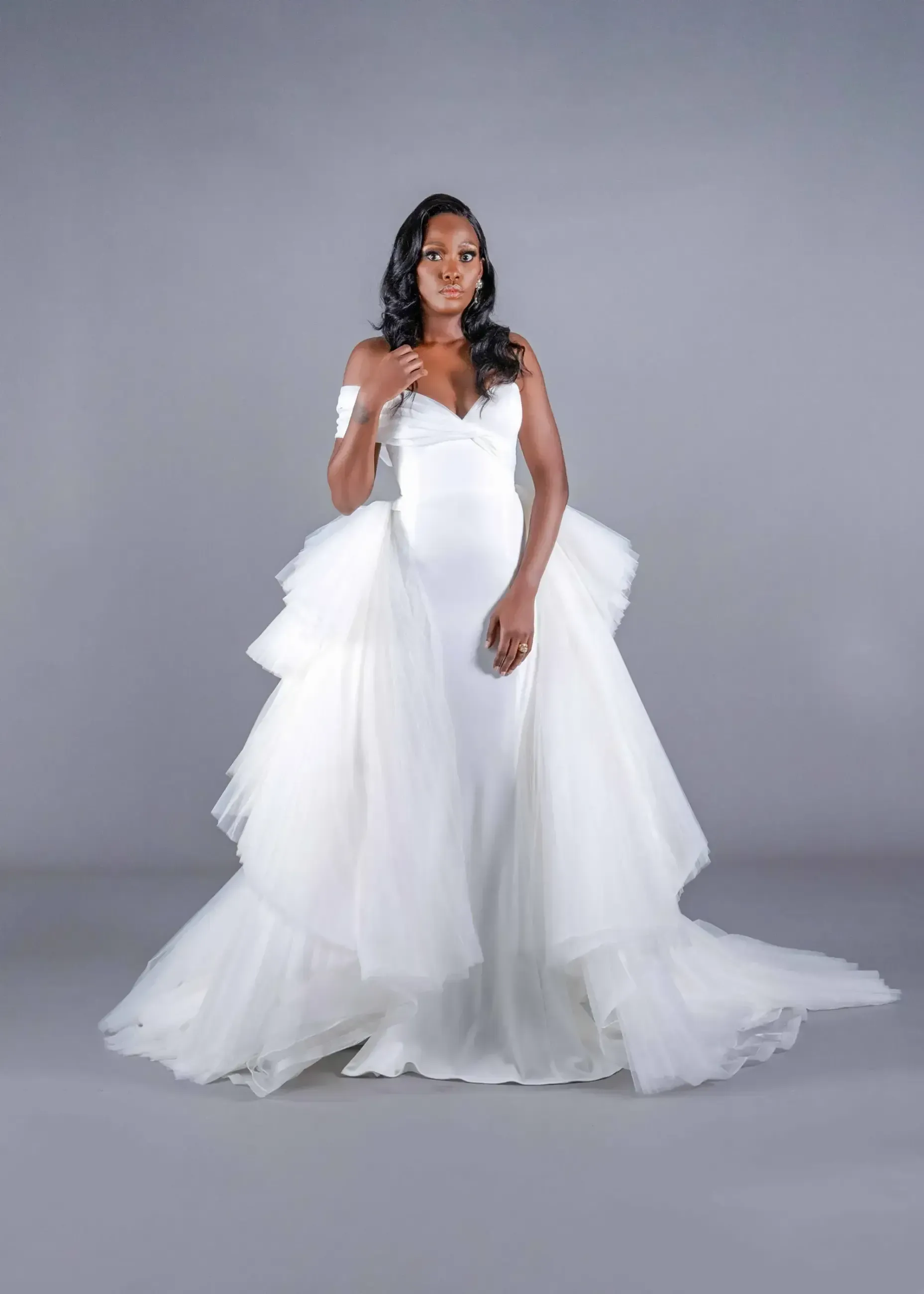 A woman in a white wedding dress is standing on a gray background.