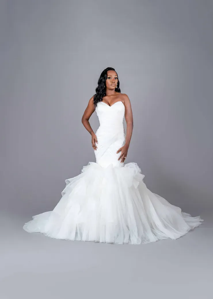 A woman in a white wedding dress is standing on a gray background.