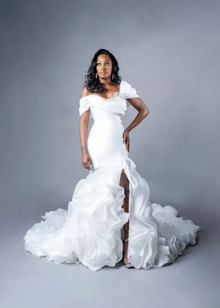 A woman in a white wedding dress is standing on a gray background.