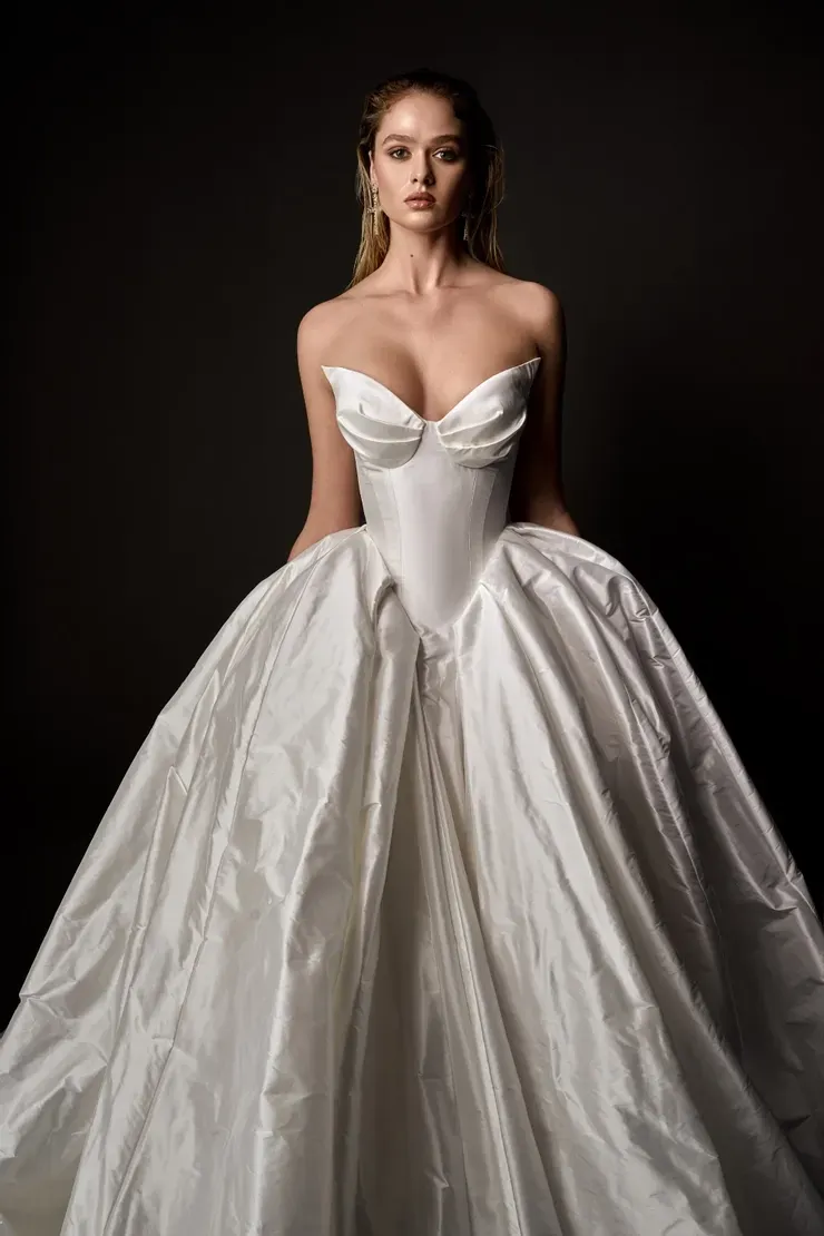 A woman in a white wedding dress is standing in front of a black background.