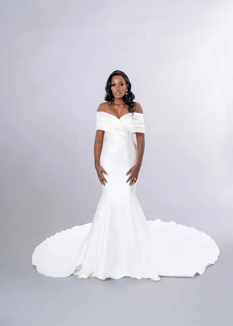 A woman in a white wedding dress is standing in front of a white background.