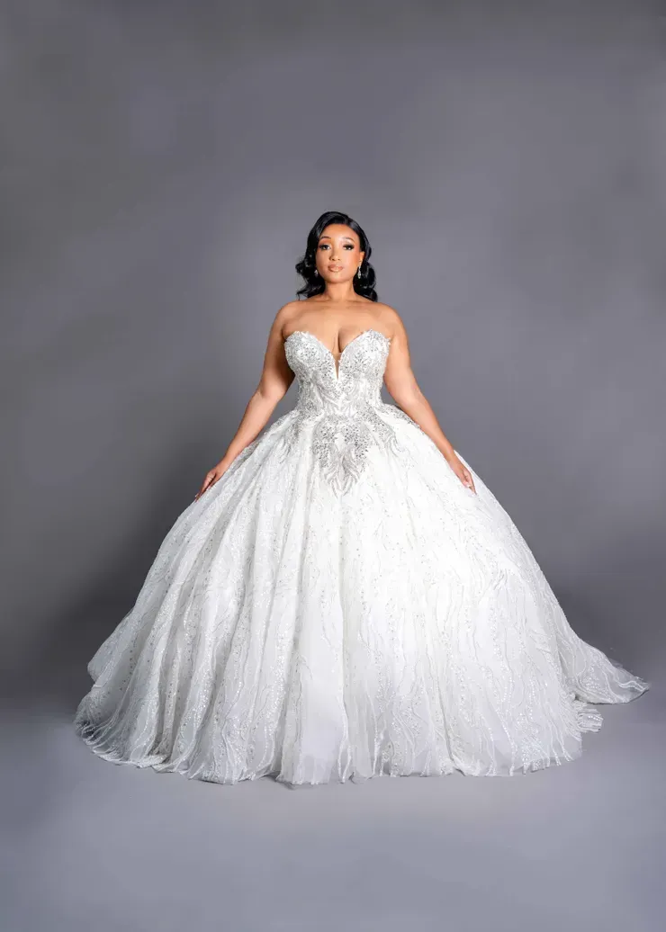 A woman in a white ball gown is standing on a gray background.