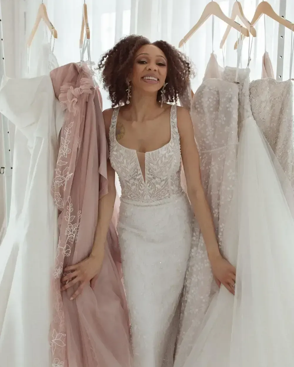 A woman in a wedding dress is standing in front of a row of wedding dresses.