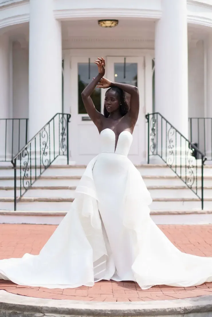 A woman in a white wedding dress is standing in front of a building.