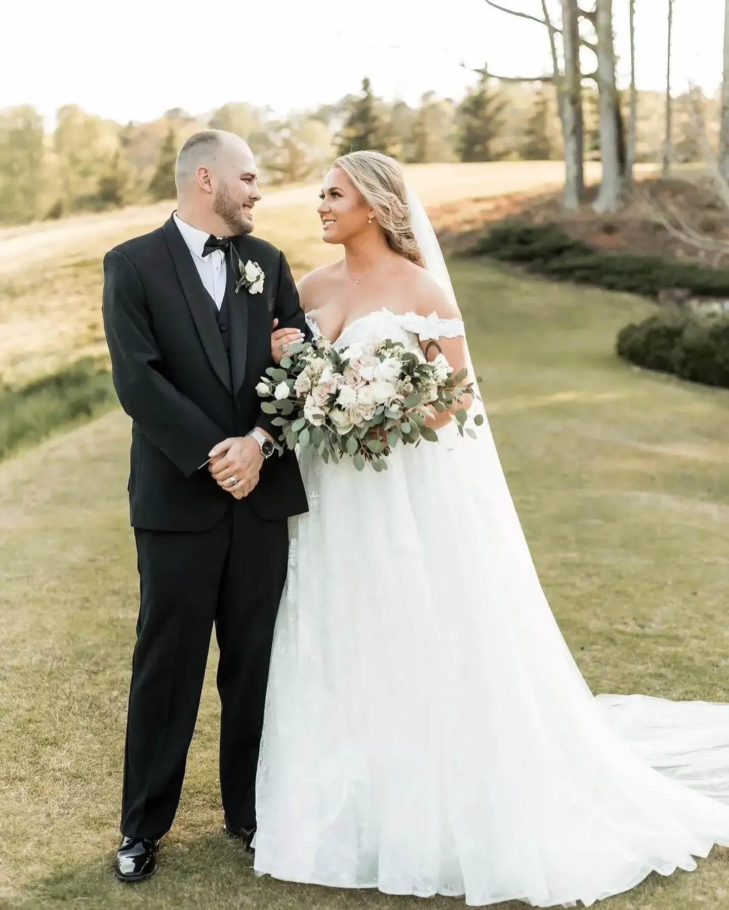 A bride and groom are standing next to each other on a lush green field.