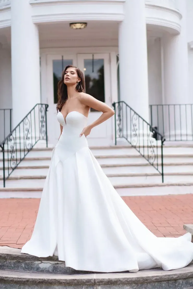 A woman in a white wedding dress is standing in front of a building.