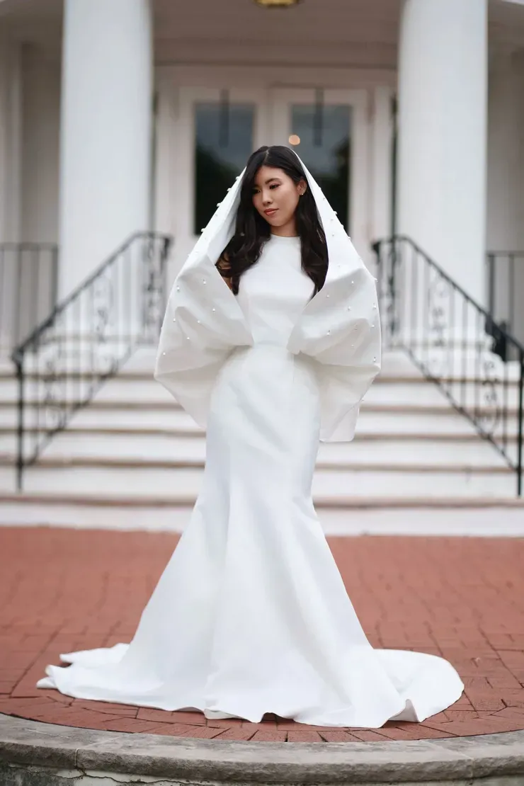 A woman in a white wedding dress is standing in front of a building.