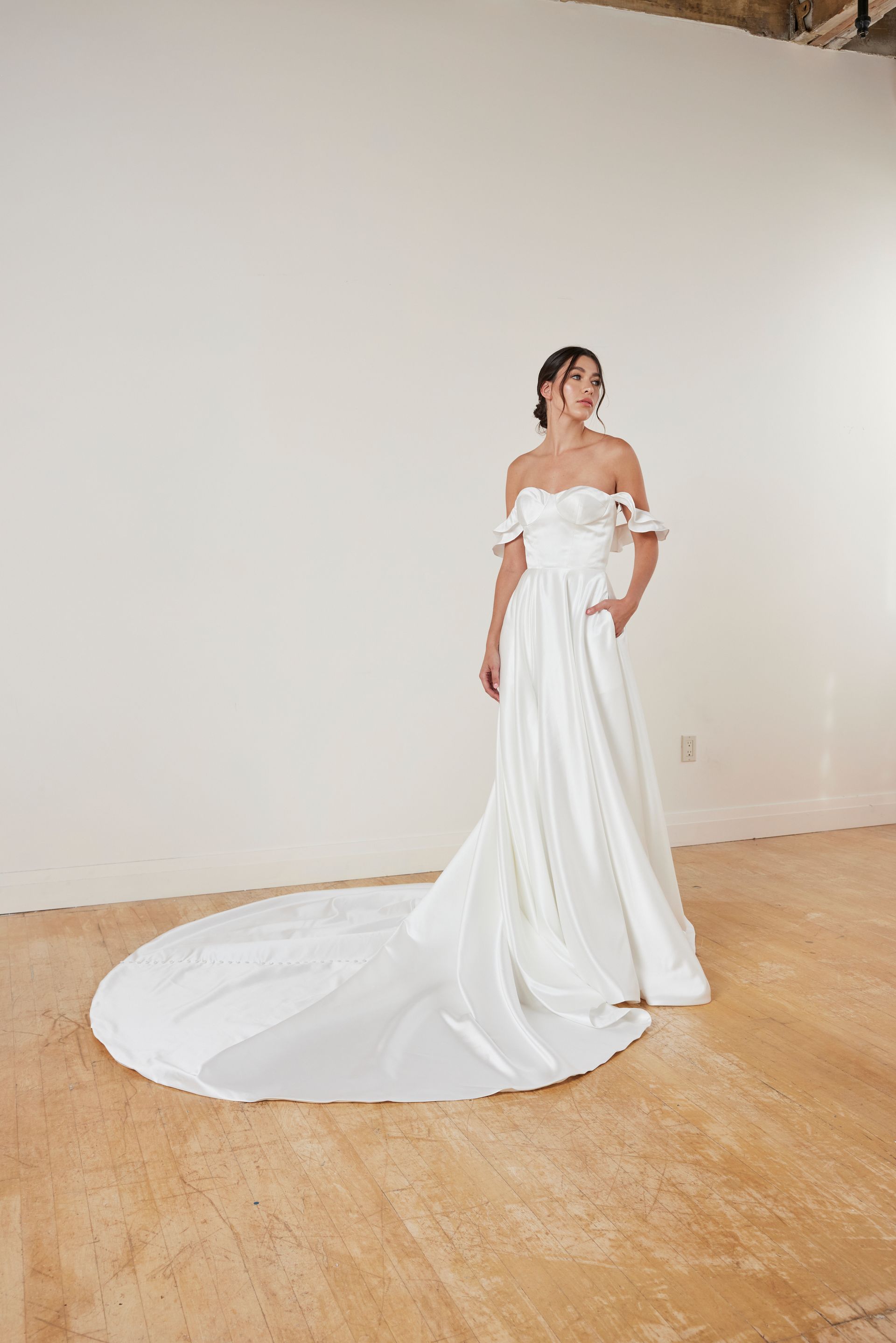 Woman in a strapless white wedding gown with a train, standing outdoors.
