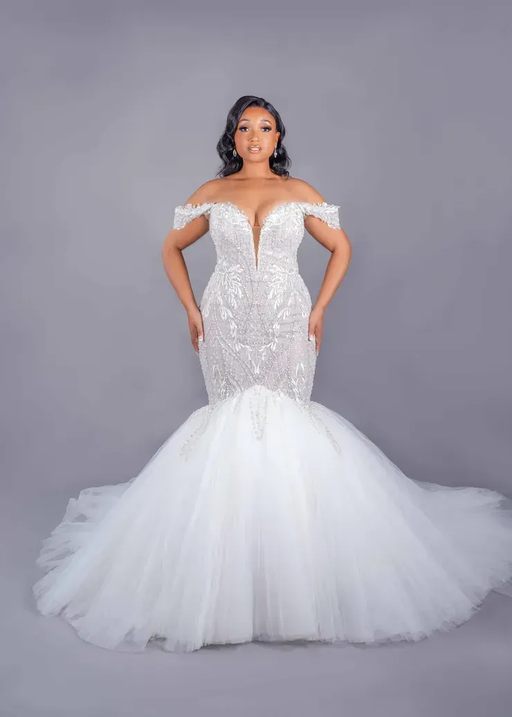 A woman in a white wedding dress is standing on a gray background.