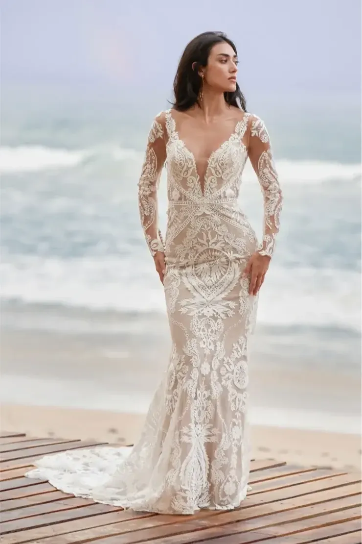 A woman in a wedding dress is standing on a pier on the beach.