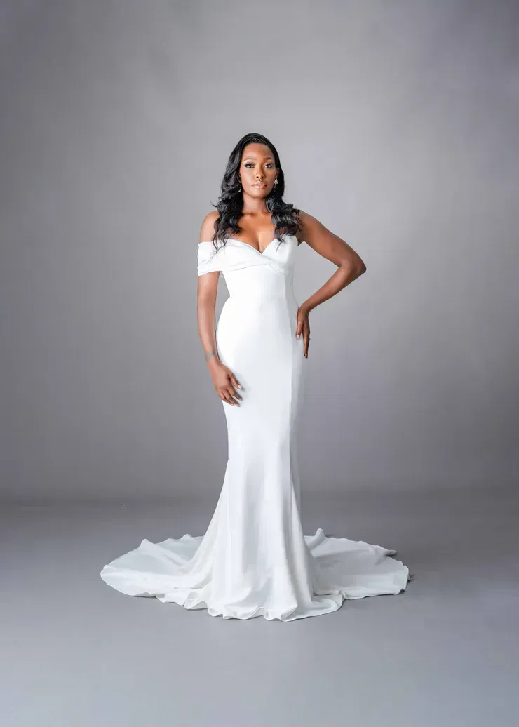 A woman in a white wedding dress is standing on a gray background.