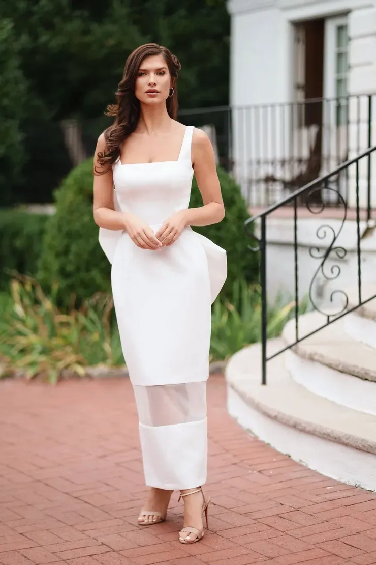 A woman in a white dress is standing in front of a white building.