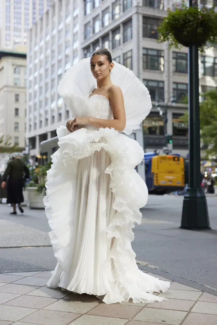 A woman in a white wedding dress is standing on a sidewalk.