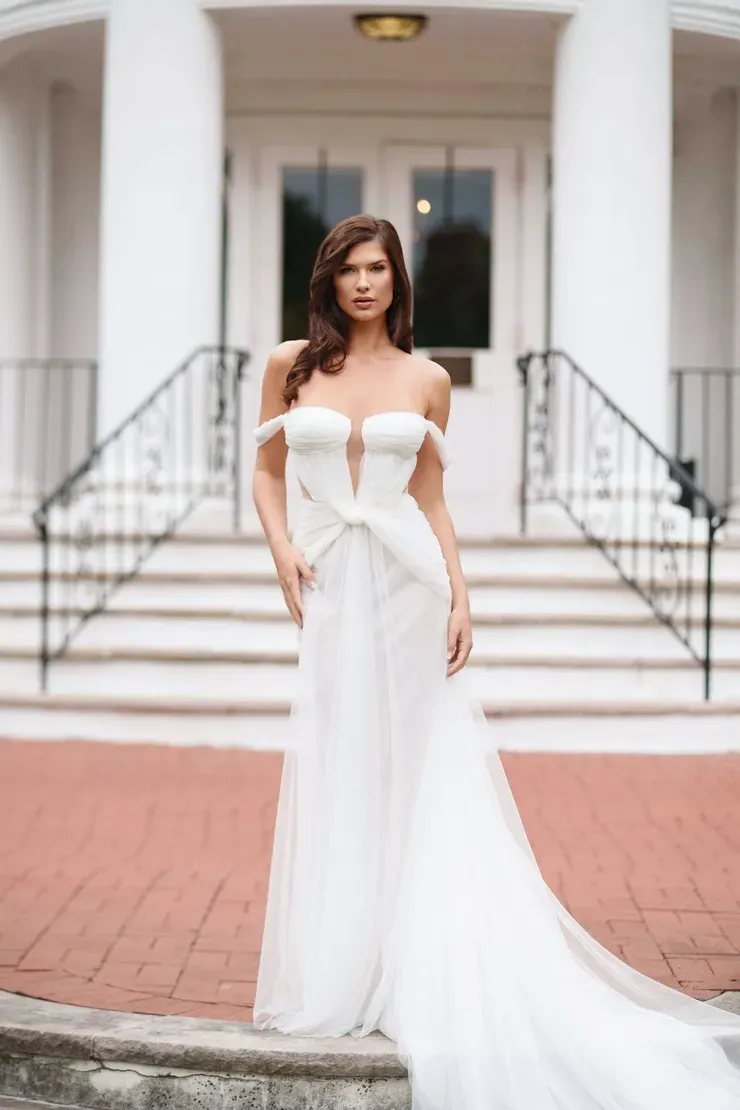 A woman in a white dress is standing in front of a building.