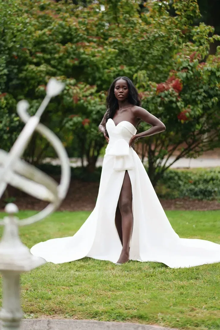 A woman in a white dress is standing in the grass in front of a sundial.