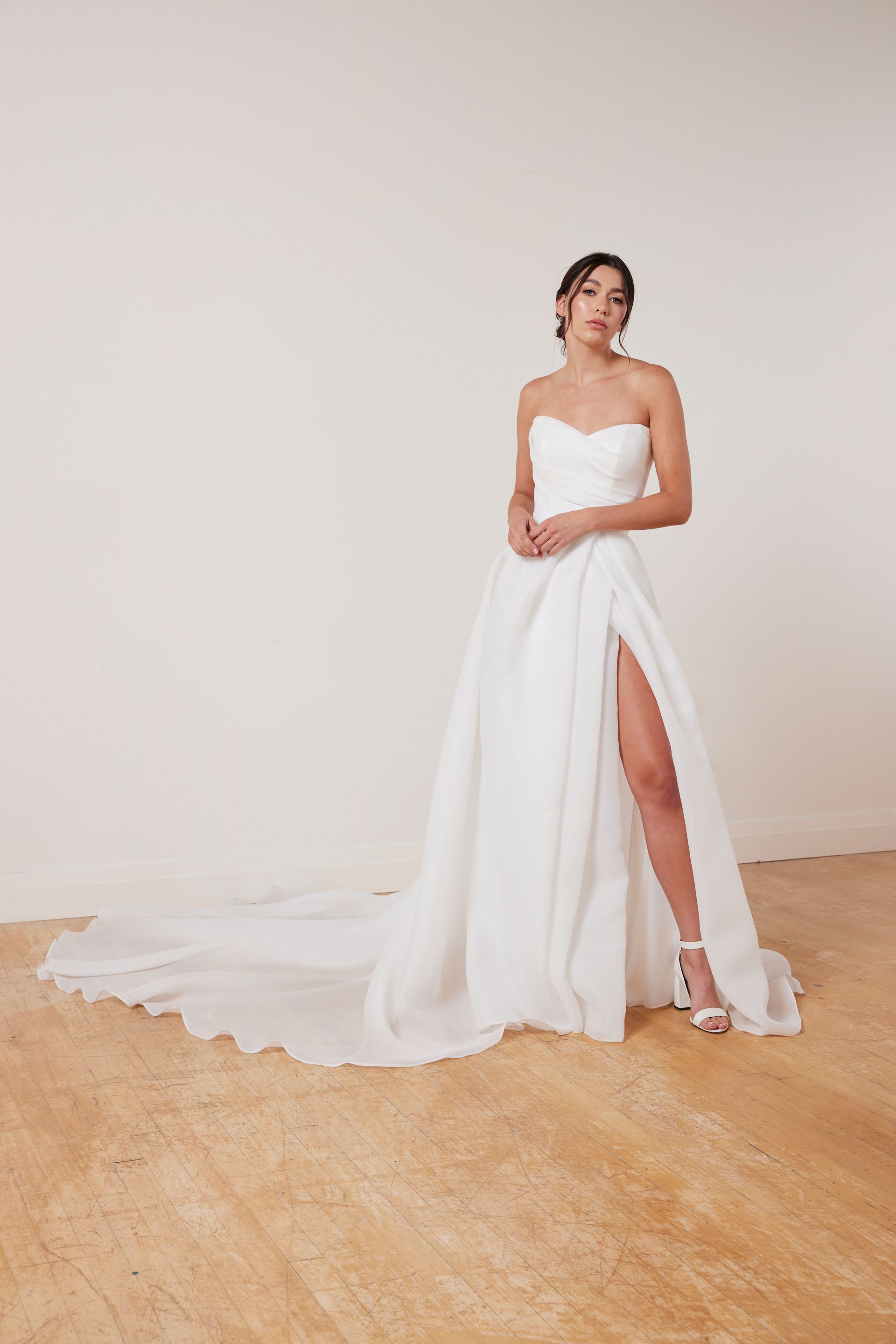 Woman in a strapless white beaded wedding gown stands by a window with a train.