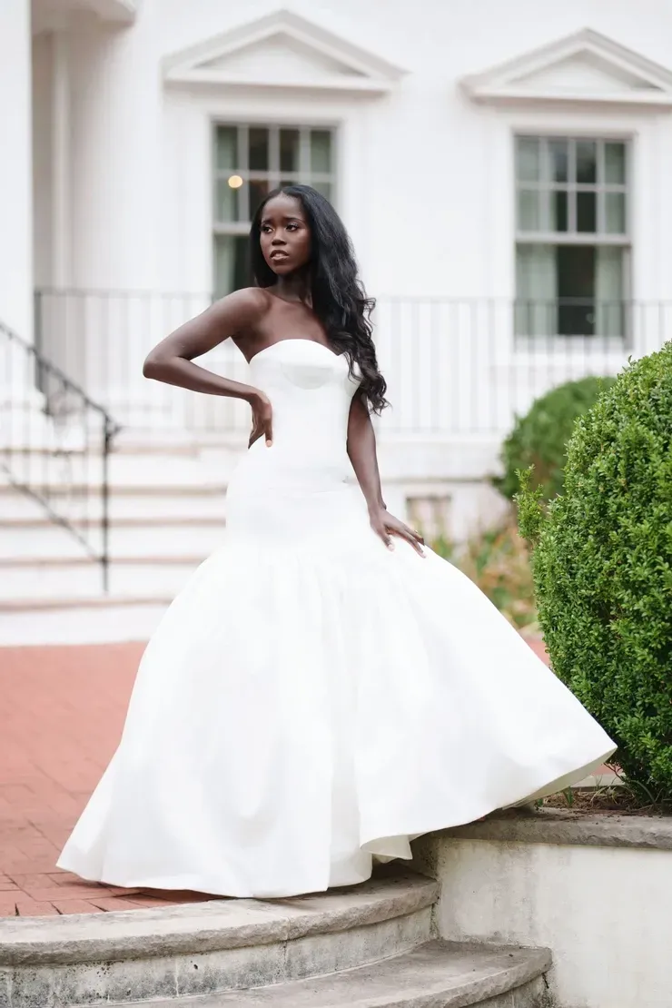 A woman in a white wedding dress is standing on stairs in front of a white building.