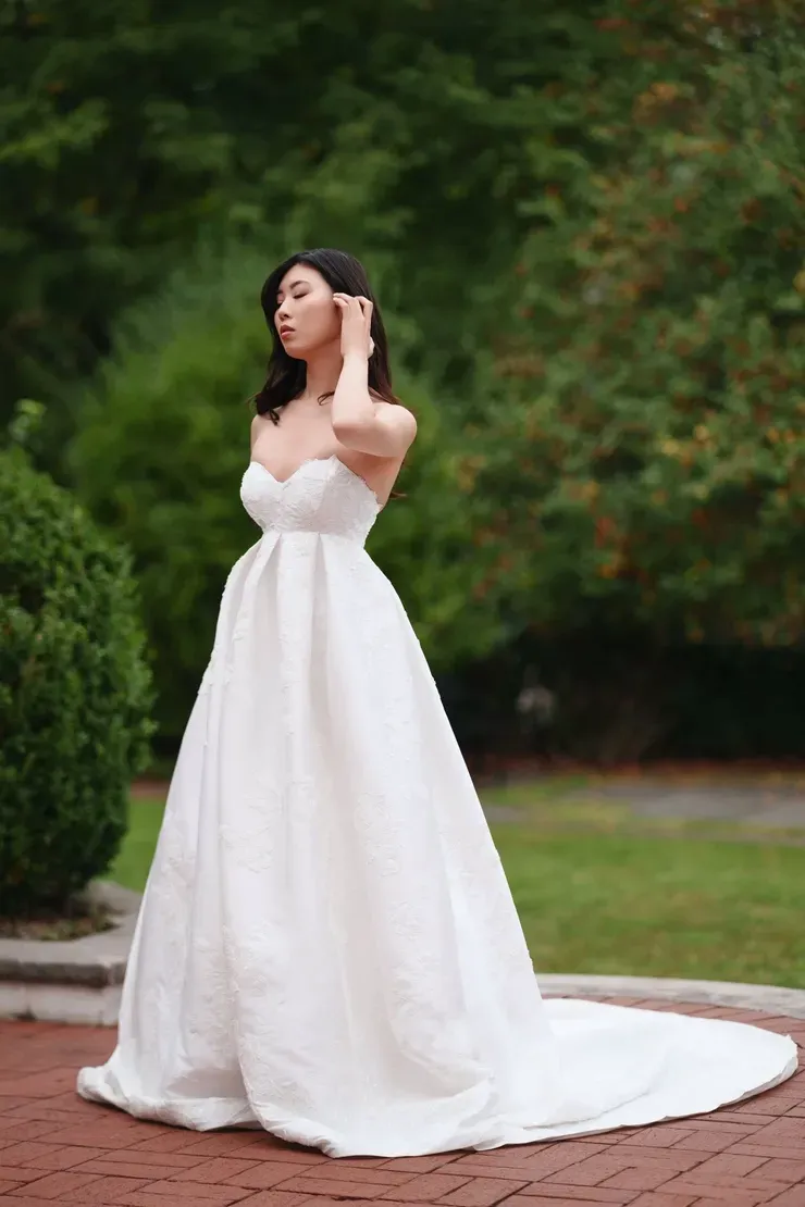 A woman in a white wedding dress is standing on a brick sidewalk.