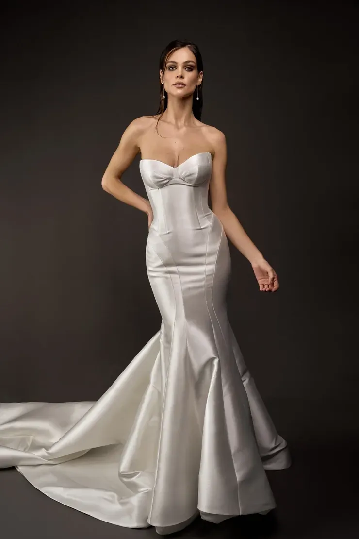 A woman in a white wedding dress is standing in front of a black background.