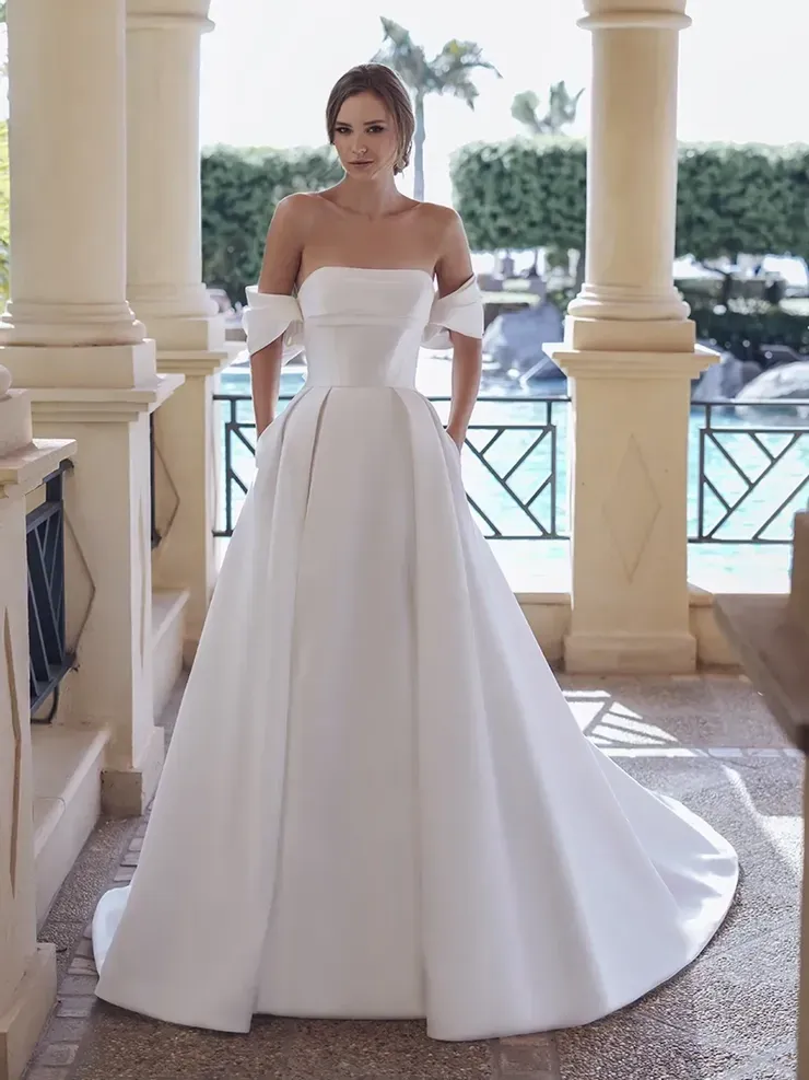A woman in a white wedding dress is standing next to a pool.